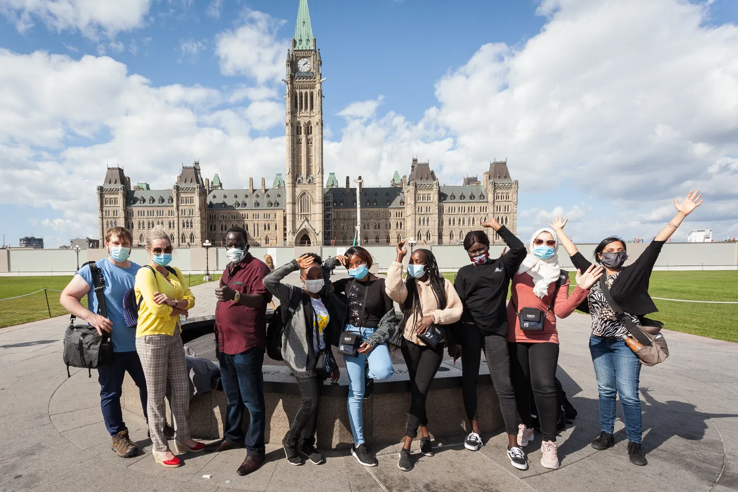 A group of people wearing masks wave in front of a large Gothic-style parliament building.