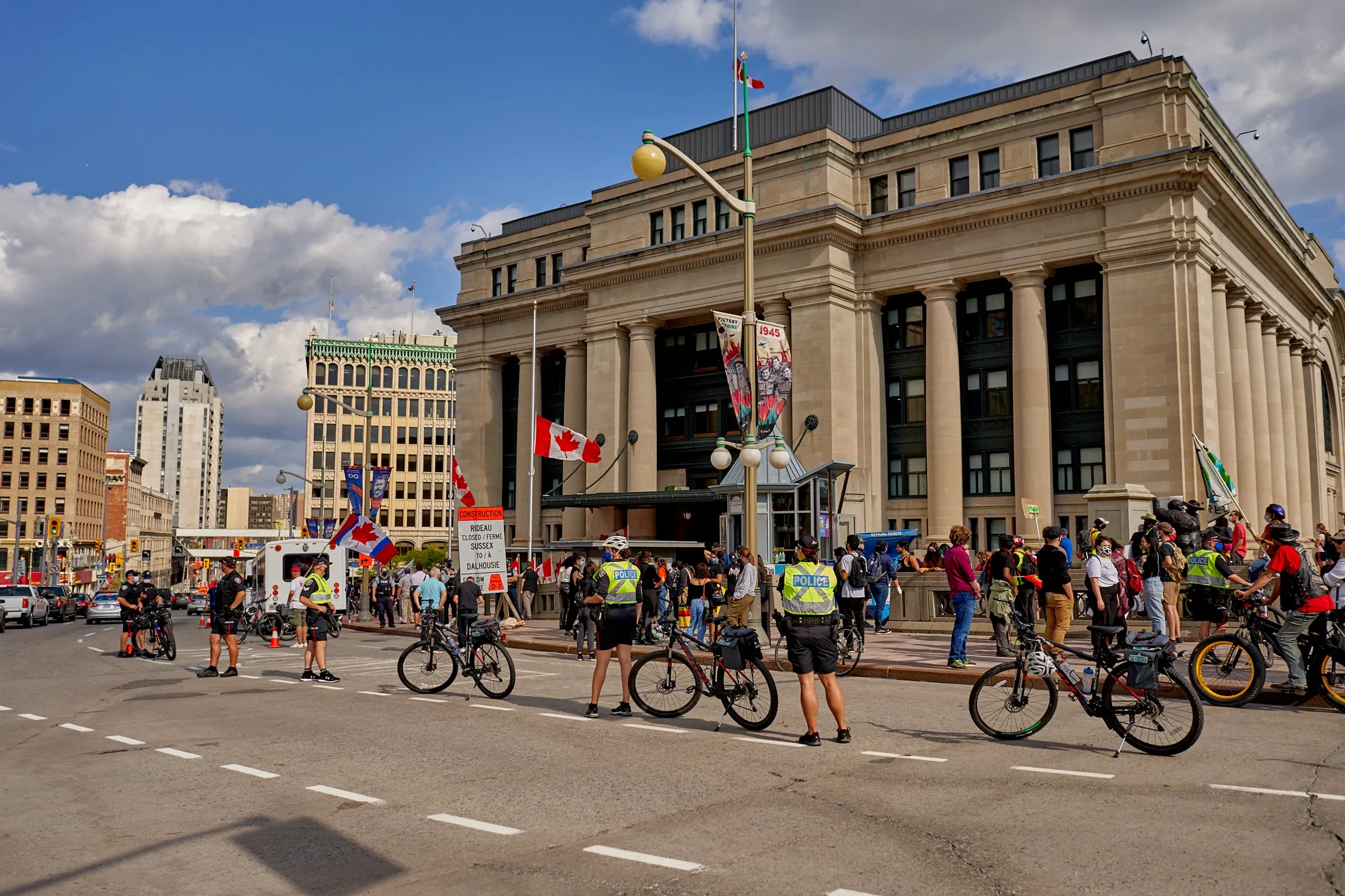 Cyclists and a crowd gather outside a large stone building on a city street.