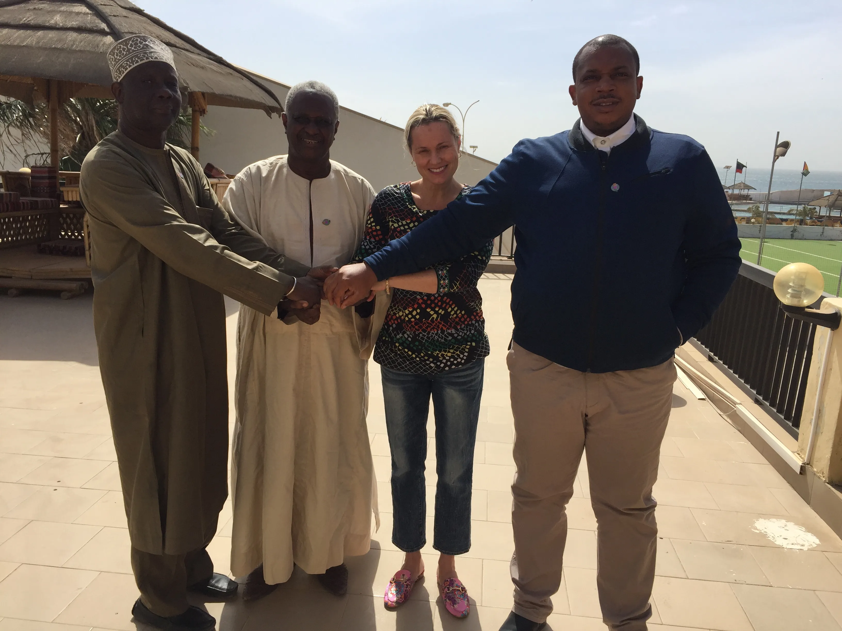 Four people stand together outdoors, joining hands in a handshake.