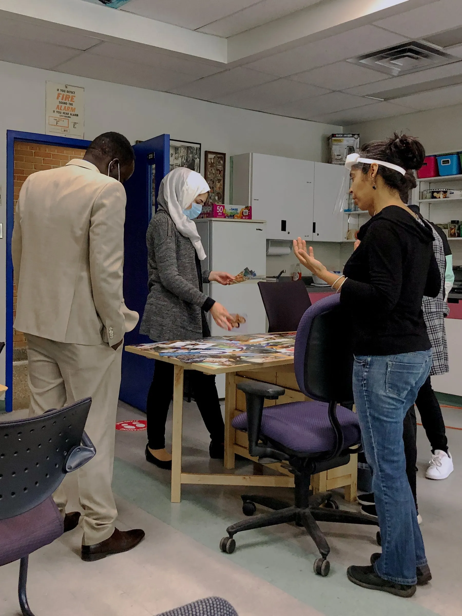 Several people gather around a table covered with papers in a classroom.