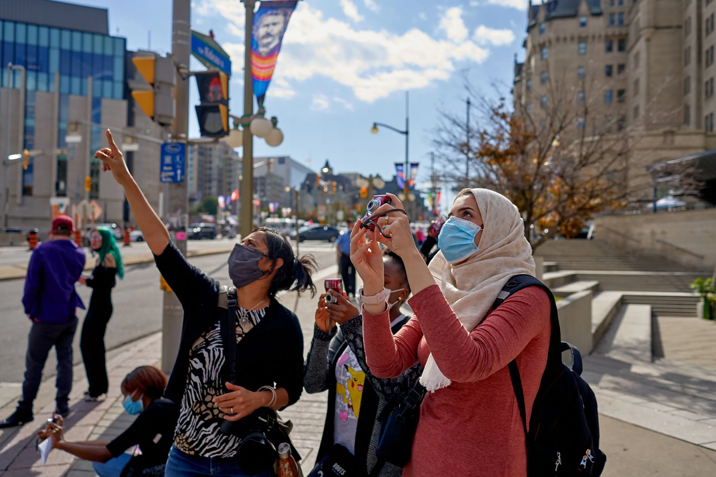 People on a city sidewalk, one pointing upward while another takes a photo.