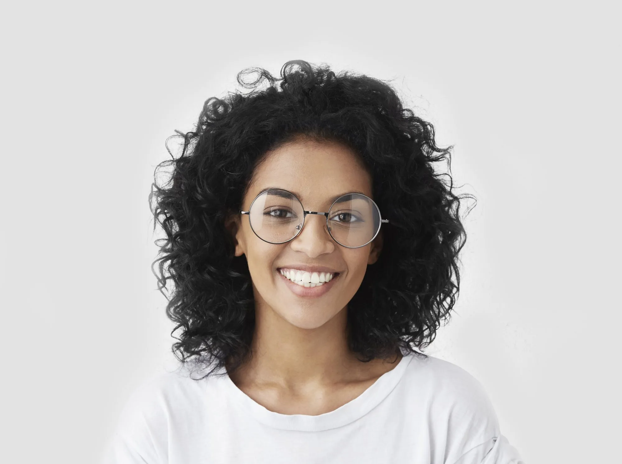 Smiling woman with curly dark hair and round glasses wearing a white shirt
